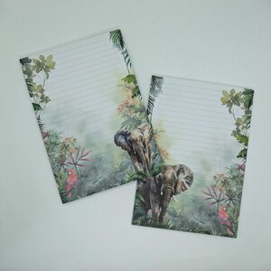 Op de afbeelding: Twee gelijnde briefpapier vellen met een junglethema. De vellen bevatten een aquarel illustratie van olifanten, weelderig groen en een papegaai. De randen van het papier zijn versierd met tropische planten en bloemen.