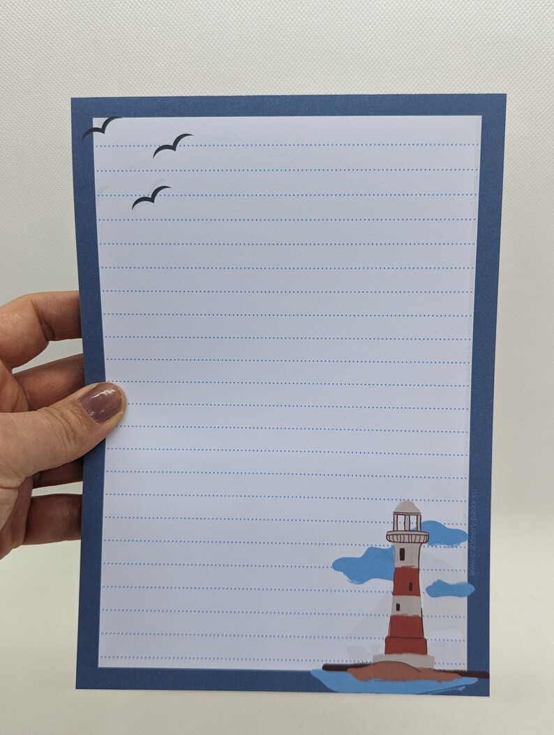 May include: Blue lined paper with a white border and a lighthouse illustration in the bottom right corner. The lighthouse is red and white with a black roof and a blue sky with white clouds behind it. There are three black birds flying in the top left corner.