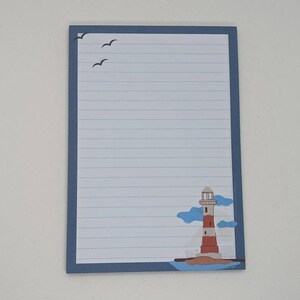 May include: A blue lined notepad with a lighthouse and seagulls on the front. The lighthouse is red and white with a blue roof. The seagulls are black.