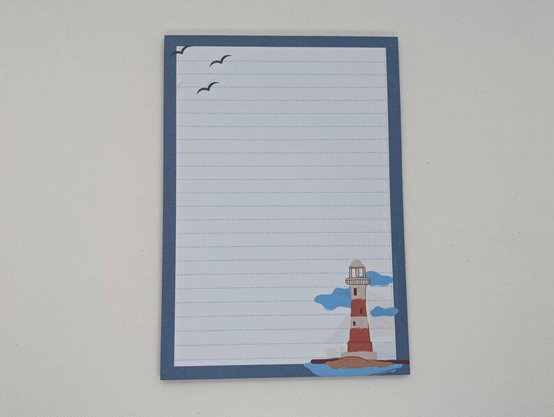May include: A blue lined notepad with a lighthouse and seagulls on the front. The lighthouse is red and white with a blue roof. The seagulls are black.