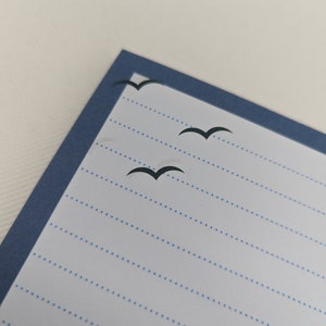 May include: A blue lined notebook with a blue border and three black bird silhouettes flying across the page.