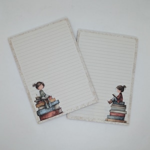 Peut inclure: Deux blocs-notes lignés avec une bordure décorative. Chaque bloc-notes présente une illustration d'une fille assise sur une pile de livres. La fille lit un livre. Les blocs-notes sont beiges et blancs.