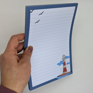 May include: A blue lined notepad with a lighthouse and seagulls illustration. The notepad has a blue border and a white background.