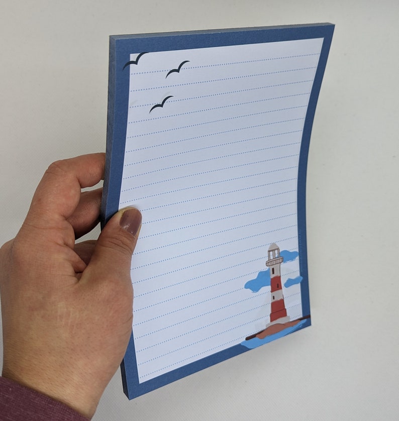 May include: A blue lined notepad with a lighthouse and seagulls illustration. The notepad has a blue border and a white background.