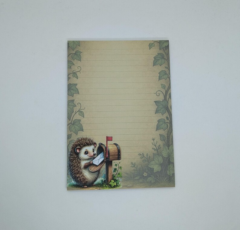 May include: A lined notepad with a whimsical illustration of a hedgehog posting a letter. The notepad features a vintage-style design with a beige background, green leaf borders, and a small mailbox.