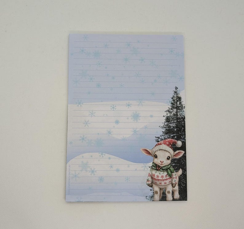 May include: A lined notepad with a winter scene featuring a lamb wearing a Santa hat and sweater. The notepad has a light blue background with snowflakes and a snowy landscape.