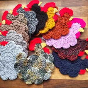 May include: A set of 12 crocheted rooster-shaped coasters in various colours, including grey, brown, purple, red, yellow, blue, and green.