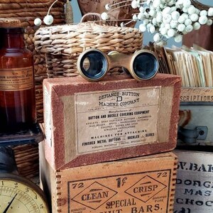 May include: A vintage scale with a brown leather-bound book labeled "ALBUM" on top. The scale is surrounded by various items, including a glass bottle, a box of peanut butter bars, a box of chocolate, and a wicker basket. The box of peanut butter bars has the text "Clean 1¢ Special Crisp Peanut Bars" on it. The box of chocolate has the text "W. Baker & Co. Dorchester Mass No. 1 Chocolate (Premium) 4-1/2 Lb Pkgs. 12 Lbs Net" on it.
