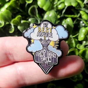 May include: Black enamel pin with a white cloud and yellow sun. The pin says "The best advice I found is don't look down".