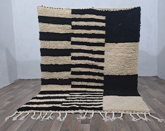 May include: A black and white geometric patterned rug with a fringe border. The rug is made of wool and has a soft, fluffy texture.