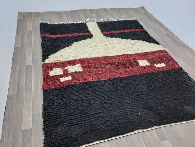 May include: A black, red, and white Moroccan rug with a geometric design. The rug has a thick pile and is made of wool.