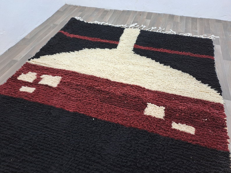 May include: A geometric patterned rug with black, white, and burgundy colors. The rug has a modern design with a large white shape in the center.