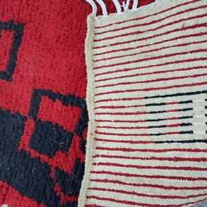 Puede incluir: Primer plano de una alfombra estampada en rojo y negro con una alfombra crema con rayas rojas y negras. La alfombra roja tiene un aspecto texturizado y peludo con formas geom&eacute;tricas. La alfombra a rayas tiene flecos.