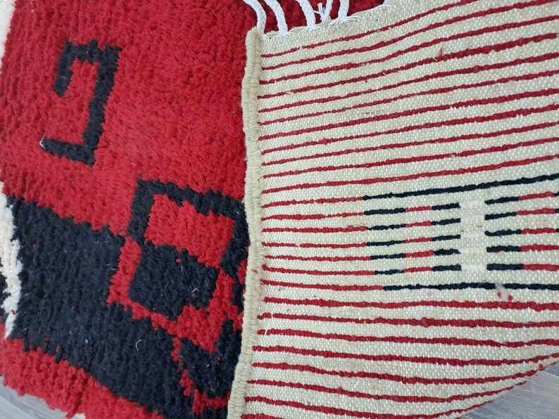 Puede incluir: Primer plano de una alfombra estampada en rojo y negro con una alfombra crema con rayas rojas y negras. La alfombra roja tiene un aspecto texturizado y peludo con formas geom&eacute;tricas. La alfombra a rayas tiene flecos.
