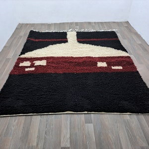 May include: A black, white, and red Moroccan rug with a geometric pattern. The rug has a thick pile and is made of wool.