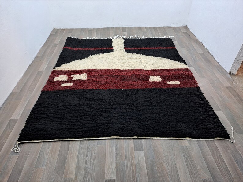 May include: A black, white, and red Moroccan rug with a geometric pattern. The rug has a thick pile and is made of wool.