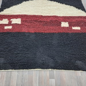May include: A black, red, and cream colored rug with a geometric pattern. The rug has a thick, textured pile.