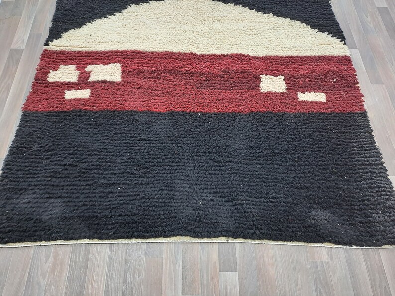 May include: A black, red, and cream colored rug with a geometric pattern. The rug has a thick, textured pile.