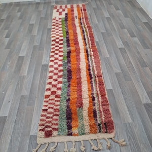 K&ouml;nnte beinhalten: Ein langer, rechteckiger Teppich mit einem farbenfrohen geometrischen Muster. Der Teppich ist aus Wolle und hat an beiden Enden Fransen. Die Farben des Teppichs umfassen Rot, Orange, Gelb, Gr&uuml;n, Blau und Lila.