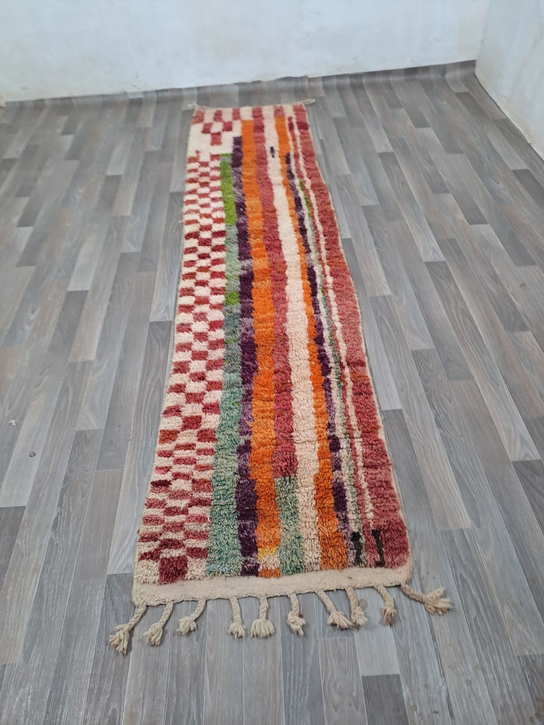 K&ouml;nnte beinhalten: Ein langer, rechteckiger Teppich mit einem farbenfrohen geometrischen Muster. Der Teppich ist aus Wolle und hat an beiden Enden Fransen. Die Farben des Teppichs umfassen Rot, Orange, Gelb, Gr&uuml;n, Blau und Lila.