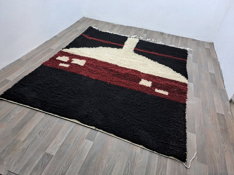 May include: A black, red, and white geometric patterned rug with a unique design. The rug is made of wool and has a soft, plush texture.