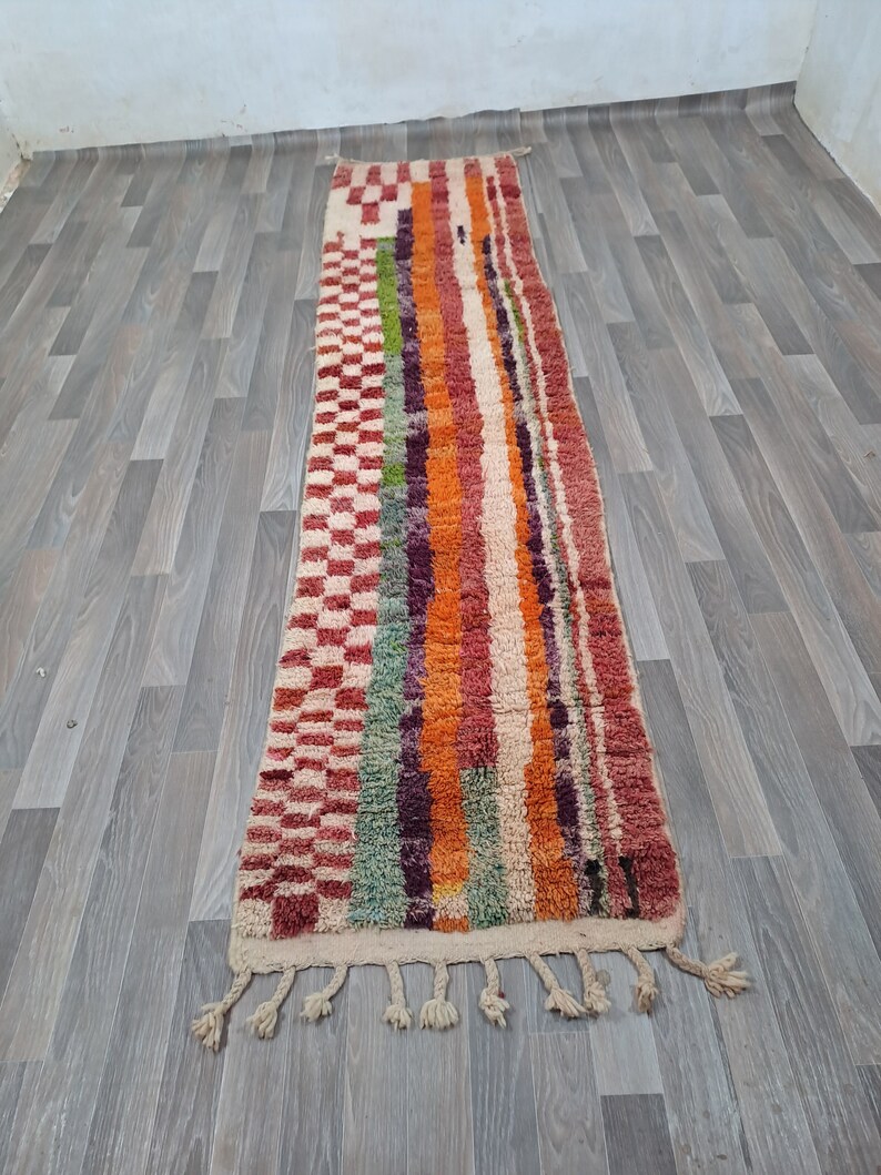 K&ouml;nnte beinhalten: Ein langer, rechteckiger Teppich mit einem bunten Streifenmuster. Der Teppich hat an beiden Enden Fransen und ist aus Wolle gefertigt. Der Teppich ist in verschiedenen Farben gehalten, darunter Rot, Orange, Gr&uuml;n, Lila und Wei&szlig;.