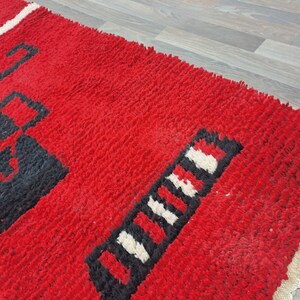 Puede incluir: Una vibrante alfombra roja con patrones geom&eacute;tricos en blanco y negro. La alfombra tiene un pelo grueso y texturizado y un borde con flecos. El dise&ntilde;o presenta formas audaces y una llamativa paleta de colores, adecuada para la decoraci&oacute;n del hogar.