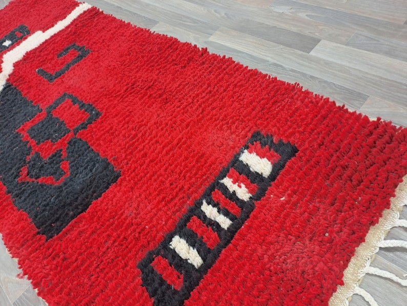 Puede incluir: Una vibrante alfombra roja con patrones geom&eacute;tricos en blanco y negro. La alfombra tiene un pelo grueso y texturizado y un borde con flecos. El dise&ntilde;o presenta formas audaces y una llamativa paleta de colores, adecuada para la decoraci&oacute;n del hogar.