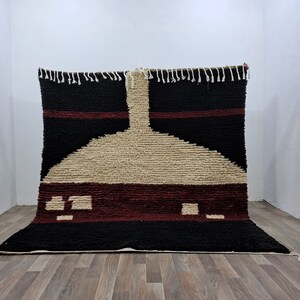 May include: A black, red, and beige Moroccan rug with a geometric design. The rug has a fringe border and is made of wool.