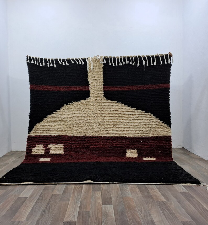 May include: A black, red, and beige Moroccan rug with a geometric design. The rug has a fringe border and is made of wool.