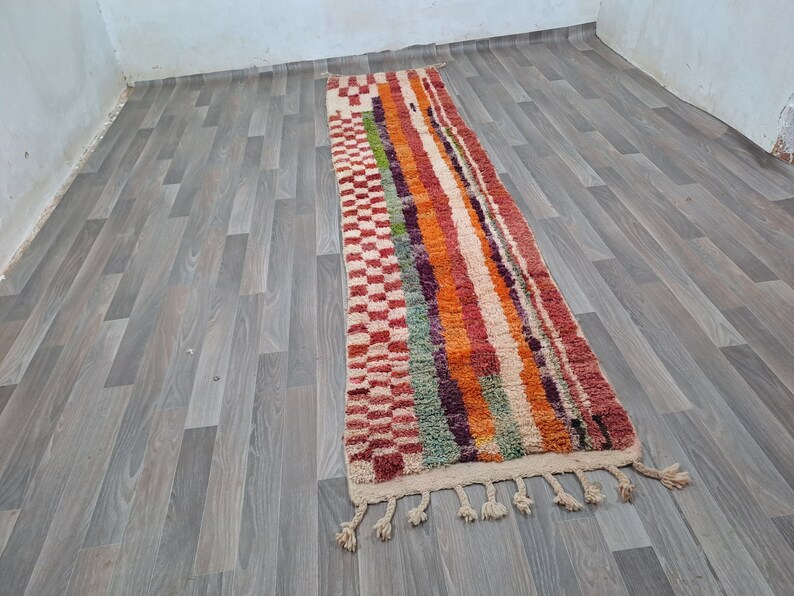 K&ouml;nnte beinhalten: Ein langer, bunter Teppich mit einem geometrischen Muster in Rot-, Orange-, Gr&uuml;n- und Violettt&ouml;nen. Der Teppich hat an beiden Enden Fransen.