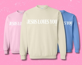 May include: Three sweatshirts with the text "JESUS LOVES YOU" in white letters on a cream colored sweatshirt, a pink sweatshirt, and a light blue sweatshirt.