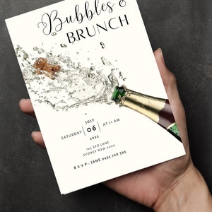 May include: A white invitation card with black text for a Bubbles & Brunch event. The invitation features a graphic of a champagne bottle with a cork popping out and a spray of bubbles. The text on the invitation includes the date, time, and location of the event. RSVP information is also included.