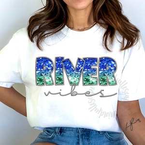 May include: White t-shirt with a blue, green, and silver sequined "River Vibes" graphic.