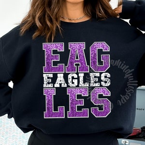 May include: Black sweatshirt featuring the word "EAGLES" in a purple glitter font. The word "EAGLES" is stacked on top of the word "EAGLES" in a white distressed font, and the word "LES" in a purple glitter font.