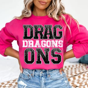 May include: Pink sweatshirt with black glitter text that reads "Drag Dragons On"