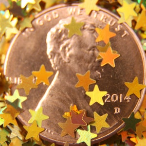 May include: A copper-colored US penny with the words "In God We Trust" and "2014 D" inscribed on it. The penny is surrounded by gold glitter stars.
