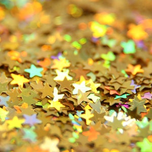 May include: A close-up of a pile of gold glitter stars. The stars are iridescent and have a variety of sizes.