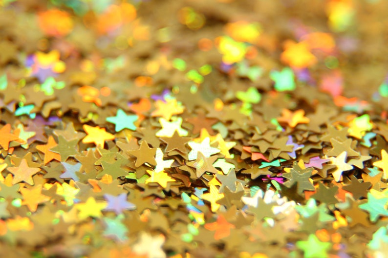 May include: A close-up of a pile of gold glitter stars. The stars are iridescent and have a variety of sizes.