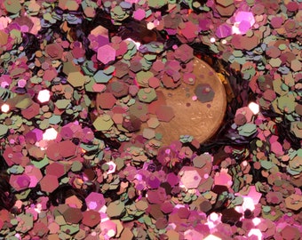 May include: A close-up of iridescent pink, green, and purple glitter with a copper coin in the center.