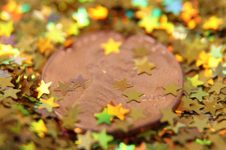 May include: A copper-colored penny coin surrounded by gold glitter stars. The coin has the year 2014 printed on it.