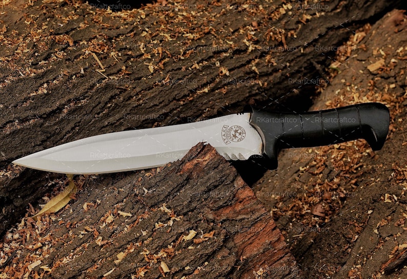 May include: A black-handled knife with a silver blade and a serrated edge. The blade has a logo engraved on it. The knife is lying on a piece of wood with wood shavings around it.