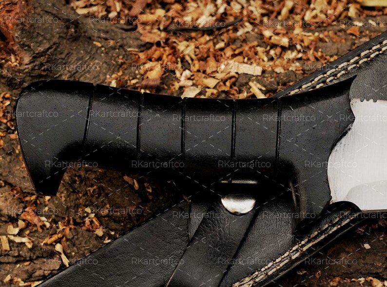 May include: A black leather sheath with white stitching detail. The sheath is partially open, revealing a black handle with a textured grip. The handle is attached to a silver metal buckle.