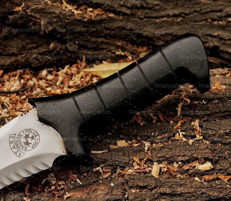 May include: A knife with a black handle and a silver blade. The blade has a serrated edge and a star-shaped design with the text "S.T.A.R.S. Raccoon Police Dept." on it.