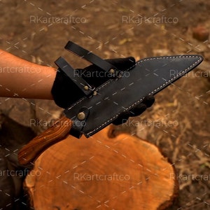 May include: A black leather sheath with a wooden handle knife. The knife is held in the hand of a person.