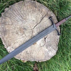 May include: A black sword with a brown handle and a cross guard. The sword is lying on a wooden stump.