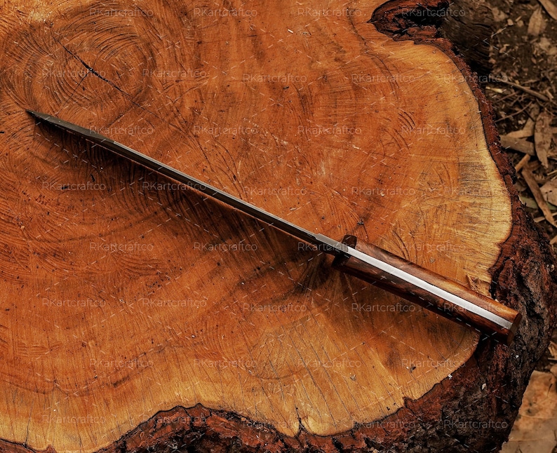 May include: A long, silver-coloured knife with a wooden handle. The knife is lying on a wooden surface.