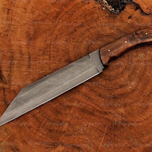 May include: A long, sharp, silver knife with a wooden handle. The handle is dark brown with a light brown grain pattern. The knife is lying on a wooden surface.