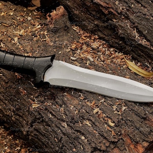 May include: A silver knife with a black handle, lying on a brown wooden surface. The knife has a sharp point and a straight edge.