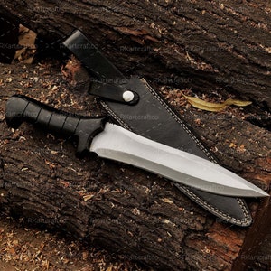 May include: A knife with a black handle and a silver blade, resting in a black leather sheath on a piece of wood.